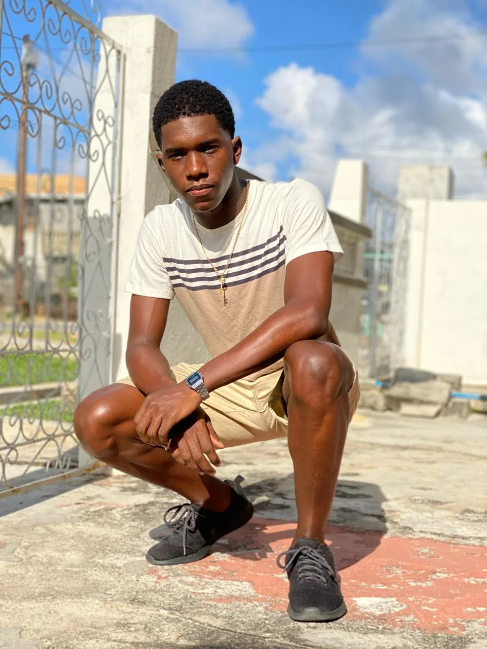 Rahsaan today, crouching by an iron gate under a blue sky